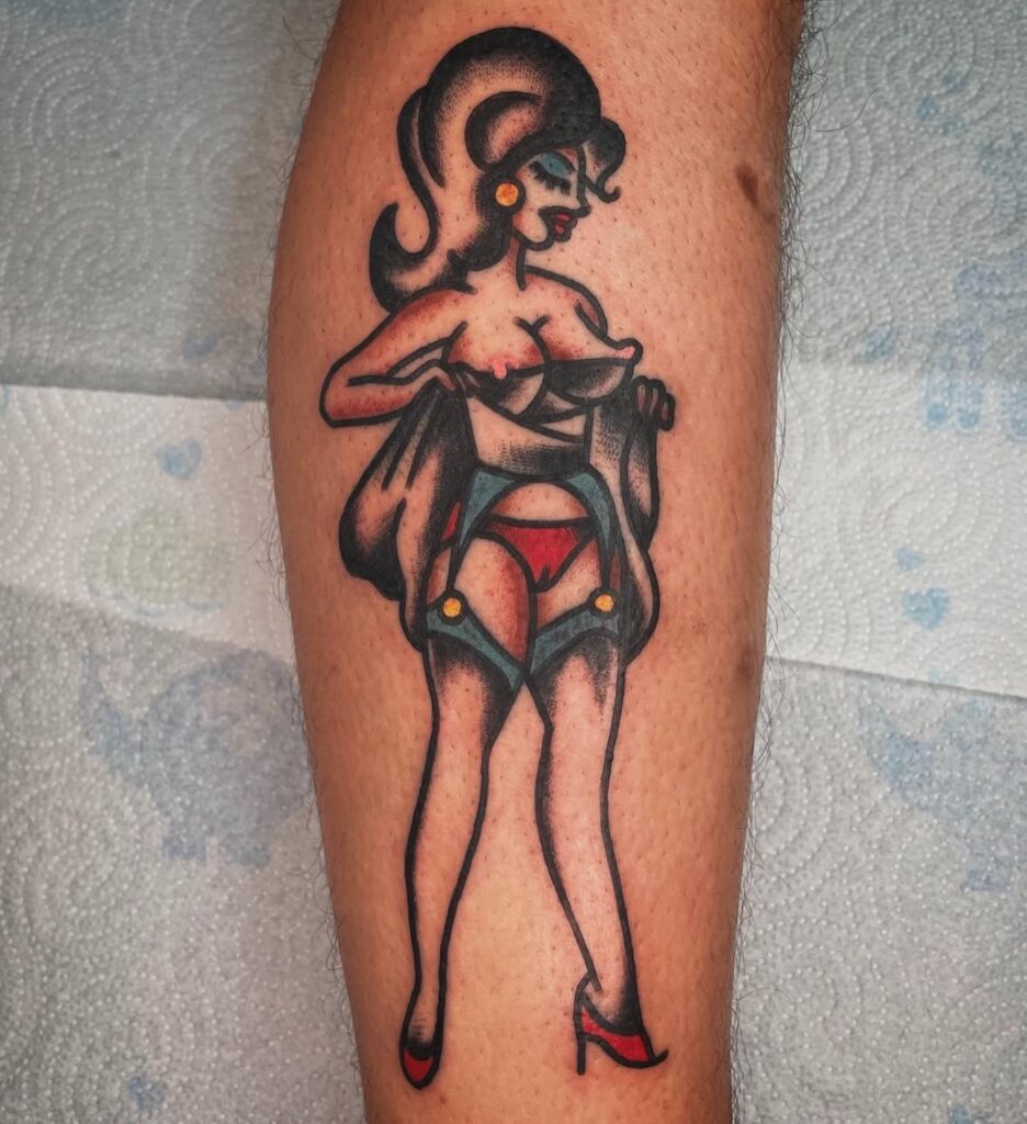 "Tatuaje estilo old school realizado en Barcelona, representando una pin-up con peinado voluminoso, tacones rojos, lencería roja y liguero azul, con líneas negras gruesas y sombreados en negro."