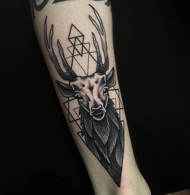 "Tatuaje en blackwork hecho en Barcelona, de un ciervo realista con fondo de triángulos geométricos en el antebrazo."
