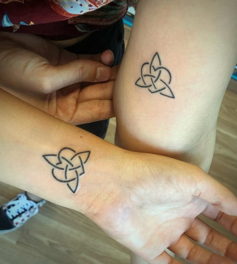 Tatuajes geométricos a juego en el brazo y la muñeca de dos personas, con un diseño de nudo celta minimalista hecho en línea negra.