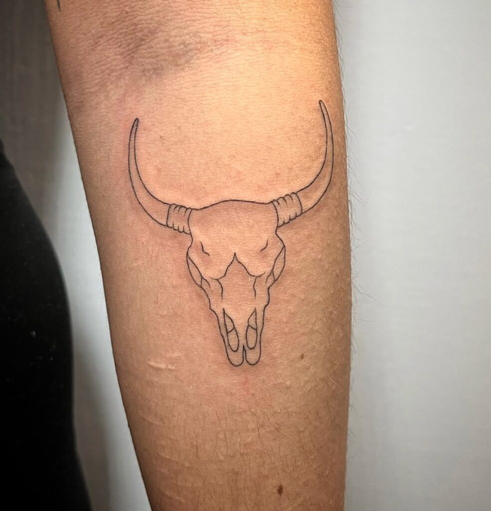 Tatuaje minimalista en línea negra de un cráneo de toro con cuernos largos, hecho en Barcelona.