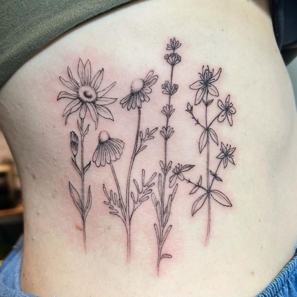 Tatuaje de flores silvestres en línea fina sobre el costado, con varios tallos y pétalos delicados, hecho en Barcelona.