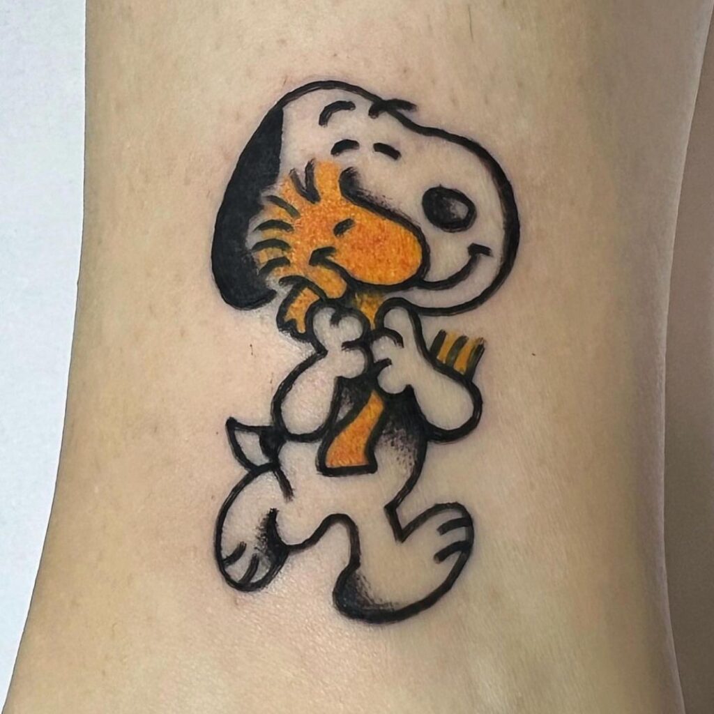 Tatuaje a color de Snoopy abrazando a Woodstock, hecho en Barcelona.