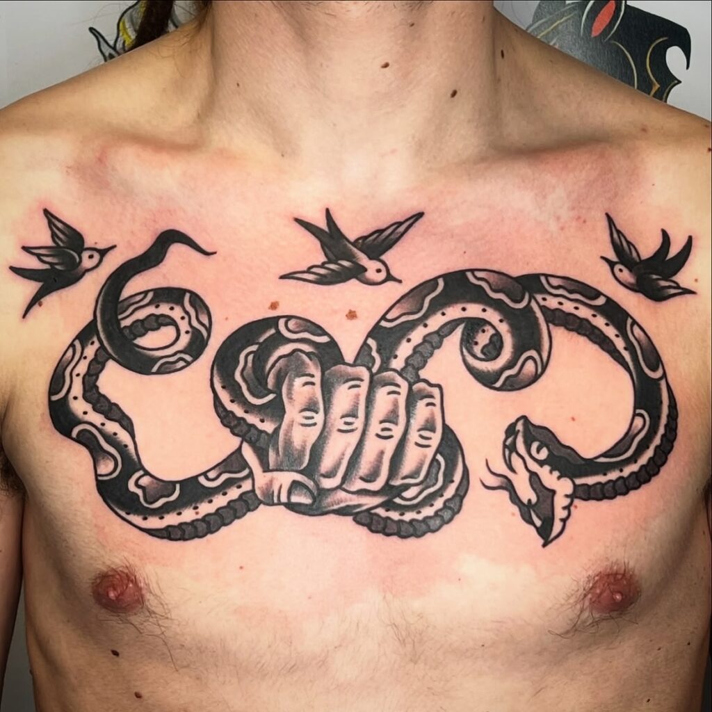 Tatuaje grande en el pecho de una serpiente enrollada alrededor de una mano con varias aves, hecho en Barcelona.