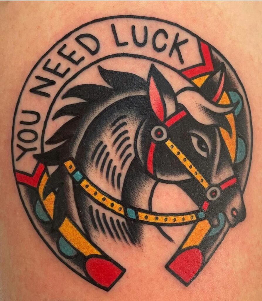 Tattoo de un caballo dentro de una herradura con la frase “You Need Luck”, en estilo tradicional americano, hecho en Barcelona.